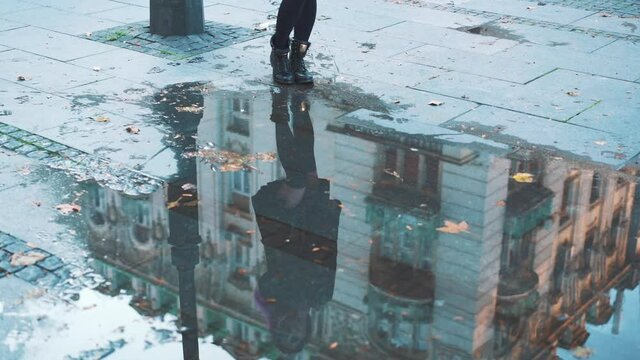 Playful carefree girl enjoying urban spring in rubber boots. female feet walking on city street pool or puddle in waterproof shoes. Woman having fun splasing water at rainy wet weather. Concept of joy