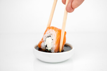 take a philadelphia maki rolls with bamboo chopsticks and put in into  soy sauce. pink ginger, wasabi on white plate, asian food, japanese cuisine background