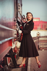 Fototapeta na wymiar Beautiful elegant young girl in vintage clothes (black coat, red shoes, white gloves) entering a historical retro train