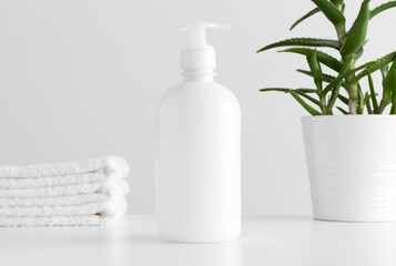 White cosmetic liquid soap dispenser bottle mockup with a aloe vera and towels on a white table.