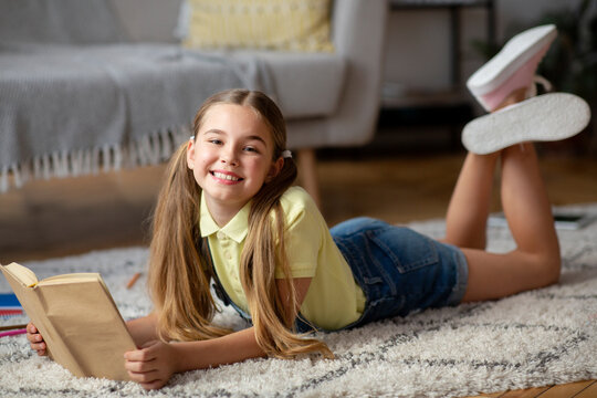 Kid lying on floor carpet, holding book, looking at camera