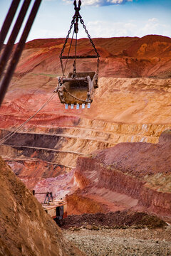 Aluminium Ore Quarry. Red Bauxite Clay Open-cut Mining. Walking Dragline Excavator Empty Bucket On Cable. Blue Sky, Clouds. Focus On Foreground.