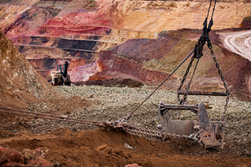 Aluminium ore quarry. Bauxite clay open-cut mining. Walking dragline bucket with empty ground. The multi-color quarry steps and excavator on background. © Alexey Rezvykh