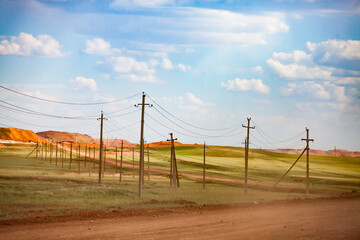 Fototapeta premium Aluminium ore quarry. Bauxite clay open-cut mining. Heaps of empty stones with green grass. Concrete poles on blue sky background.