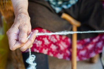 Close-up of an old woman's hands as she winds a woolen thread used to make traditional products in Serbia, woolen socks, sweaters and vests made of natural wool