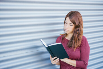 Fototapeta premium young girl reading at a cover black book on the street