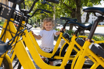 little girl is standing next to bicycle to rent in the parking lot in the city.