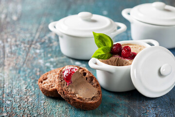 Fresh homemade chicken liver pate with cranberry sauce in ceramic serving pans and slices keto bread, selective focus