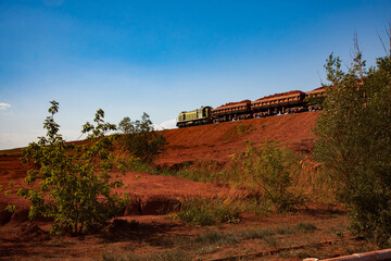 Bauxite clay open-cut mining. Hopper car train with aluminium ore. Blue sky background. Evening light on sunset