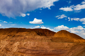 Bauxite clay open cast (open cut) mining. Color aluminium ore quarry. Big yellow heaps of empty rocks. Slag heaps. On blue sky with clouds.