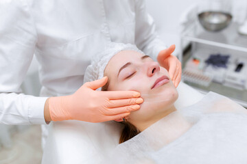Fototapeta na wymiar Hands of skillful beautician cleaning and touching female face with cotton pad or sponge in the white office. Facial skincare. Beautiful caucasian woman on a cosmetology procedure. wellness center