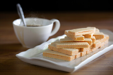 Wafers in white dish and black coffee in white cup which has stain of coffee all on brown wooden table