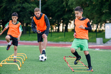 Two school boys are running ladder drills on the turf during football summer camp. Intense soccer...