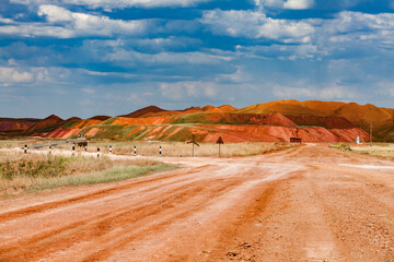 Landscape of bauxite mine (aluminium ore quarry). Orange clay soil and blue sky with clouds. Dump heaps and road with road signs. Blue sky with cloud.