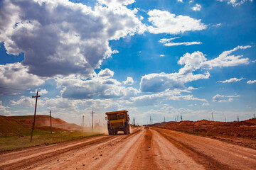 Aluminium ore quarry (bauxite clay mine). Dump truck on dusty orange road. Blue sky with clouds background. © Alexey Rezvykh