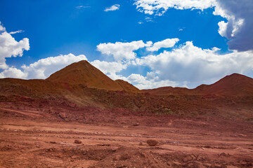 Aluminium ore quarry. Bauxite clay open-cut mining. Heaps of empty rocks. Blue sky with clouds and road.