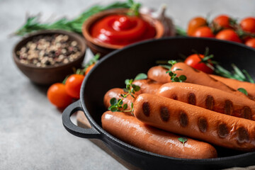 Roasted sausages in cast-iron frying pan over concrete background.