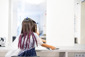 little girl dyes her hair purple in a hairdressing salon