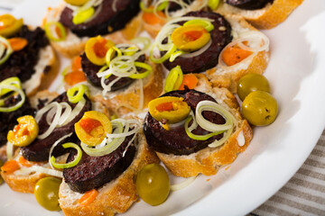 Fototapeta na wymiar Delicious canapes with fried morcilla (blood sausage with rice) and green olives..