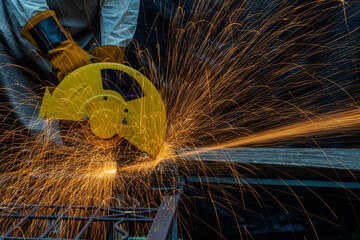 Hands of man with glove using electric steel cutter machine while working at workshop. Male cutting steel with sparks flying. Hard work in factory or garage industry in construction site concept.