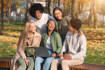 Cheerful friends having fun at public park, using laptop