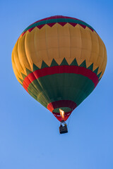 Fototapeta premium A bright multicolored hot air balloon with an expansive burner flame soars up against a background of blue sky. Colorful balloon watercolor painting. Close-up.