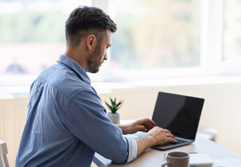 Fototapeta premium Busy Male Entrepreneur Working On Laptop With Black Screen In Office