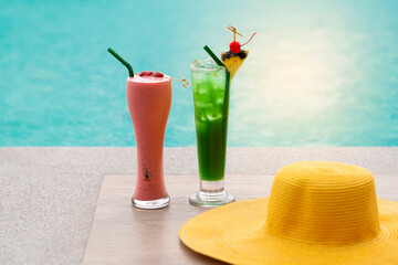 Fresh glass of Raspberry smoothie and Green cocktail with pineapple slices and straw hat on border of a swimming pool with beautiful sunlight.