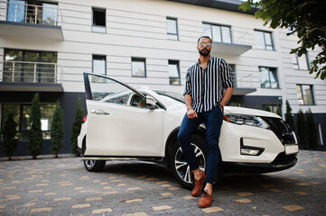 Successful arab man wear in striped shirt and sunglasses pose near his white suv car. Stylish arabian men in transport.
