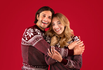 It's Christmas. Affectionate young couple in winter clothes hugging over red background