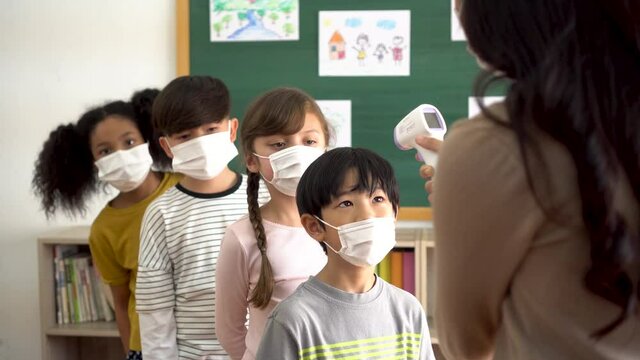 Group of diverse students in school building checked and scanned for temperature check. Elementary pupils are wearing a face mask and line up before entering into classroom. Covid-19 school reopen.