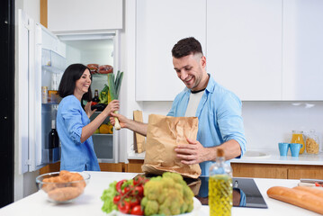 Young stylish couple unpacking together fresh products from market in cozy kitchen.