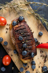 Goose breast Christmas roast with blueberries, tomatoes, red peppers and rosemary served on a wooden board