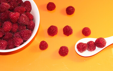 Ripe raspberries in a white plate on an orange background. On a white spoon raspberries.