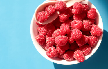 Ripe raspberries in a white plate on a blue background. On a white spoon raspberries.