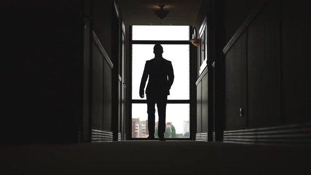 Unrecognizable businessman in formal wear looking into skyscraper window. Silhouette of successful man walking through office hall. Confident male entrepreneur at work. Low angle view Slow motion