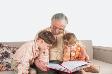 Positive elderly man reading a book for his grandchildren sitting on sofa.