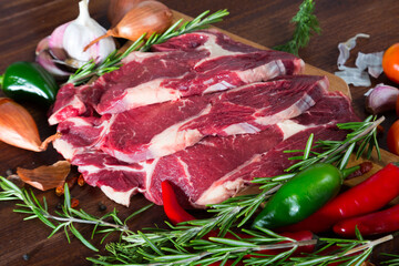 Raw beef steaks with rosemary and vegetables assortment on natural wooden desk, cooking ingredients