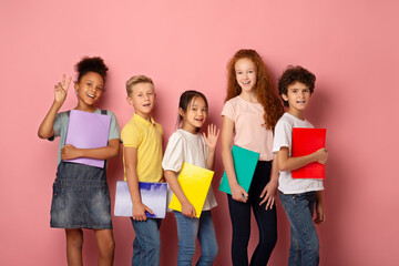 Portrait of happy school students with copybooks smiling on pink background