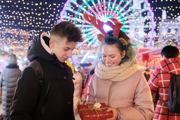 Couple of young people at Christmas market. Happy boy and girl giving gift box