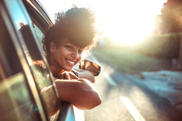 Beautiful curly hair woman enjoying the breeze, looking out of the window's car while having a road trip - obrazy, fototapety, plakaty