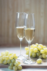 Two glasses with sparkling wine and grapes on light wooden background. Selective focus.