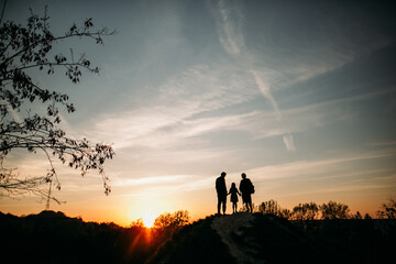 
family with daughter look at the sunset in autumn, their silhouettes stand on a slide in the park