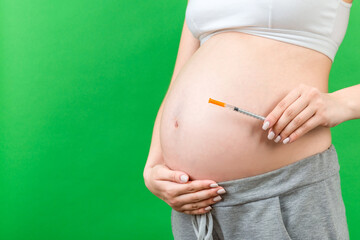 Close up of pregnant woman holding insulin syringe against her belly at colorful background with copy space. Diabetes concept