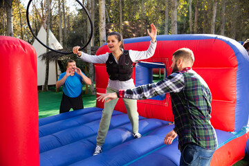 Fototapeta na wymiar Emotional woman trying to put on hoop on log on inflatable playground, male friends watching