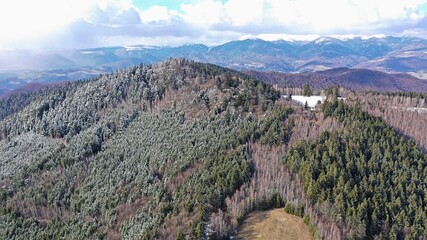 Fototapeta premium Aerial view of forested hills under High Tatra mountains during first winter snow in mountains. Mixed forests contains mostly spruce trees and various naked broadleaf trees.