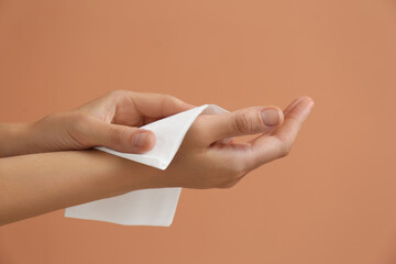 Woman cleaning hands with paper tissue on light brown background, closeup