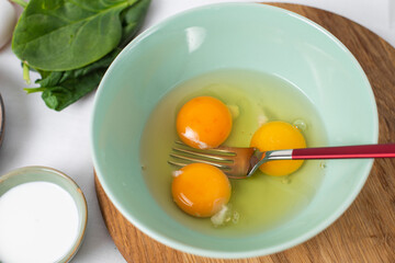 The process whisking egg yolks, making tasty egg omelet with green spinach for breakfast on white background. Idea recipe for a healthy diet food. Easy to cook. Protein food for a vegetarian.