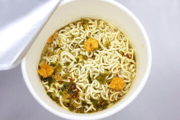 instant noodles, noodle soup in a cup, view from above. Instant noodles are sold in a precooked and dried noodle block, with flavoring powder and/or seasoning oil.