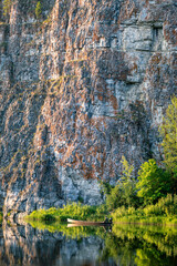 Obraz premium A picturesque landscape with rocks along the river and a fisherman in a wooden boat in the summer season. Ural, Chusovaya river.